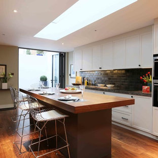 This is an example of a medium sized contemporary single-wall kitchen in London with recessed-panel cabinets, medium hardwood flooring, an island and brown floors.
