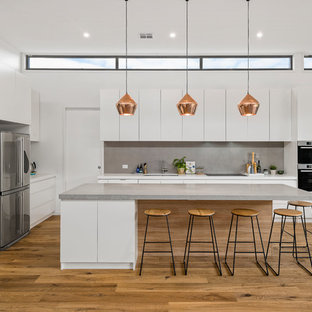 This is an example of a contemporary l-shaped kitchen in Melbourne with an undermount sink, flat-panel cabinets, white cabinets, grey splashback, stainless steel appliances, medium hardwood floors, with island, brown floor and grey benchtop.