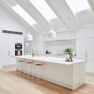 Large contemporary open concept kitchen ideas - Open concept kitchen - large contemporary galley light wood floor, beige floor and tray ceiling open concept kitchen idea in Melbourne with an undermount sink, shaker cabinets, white cabinets, quartz countertops, white backsplash, quartz backsplash, stainless steel appliances, an island and white countertops
