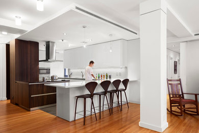 Example of a large trendy u-shaped medium tone wood floor kitchen design in New York with flat-panel cabinets, white cabinets, stainless steel appliances, white backsplash and a peninsula