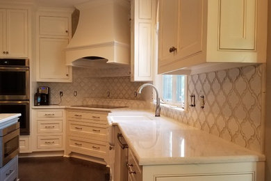 Inspiration for a medium sized traditional l-shaped enclosed kitchen in Nashville with a belfast sink, recessed-panel cabinets, white cabinets, engineered stone countertops, white splashback, porcelain splashback, stainless steel appliances, dark hardwood flooring, an island and brown floors.