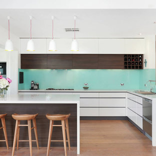 This is an example of a large contemporary l-shaped kitchen in Sydney with stainless steel appliances, white benchtop, a drop-in sink, flat-panel cabinets, white cabinets, blue splashback, medium hardwood floors, a peninsula and brown floor.
