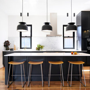 This is an example of a mid-sized transitional single-wall kitchen in Sydney with black cabinets, white splashback, marble splashback, stainless steel appliances, light hardwood floors, with island, brown floor and recessed-panel cabinets.