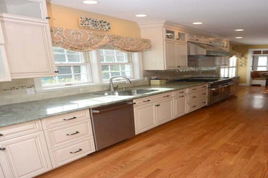 Open concept kitchen - mid-sized traditional galley medium tone wood floor and brown floor open concept kitchen idea in Boston with an undermount sink, raised-panel cabinets, white cabinets, granite countertops, beige backsplash, ceramic backsplash, stainless steel appliances and an island