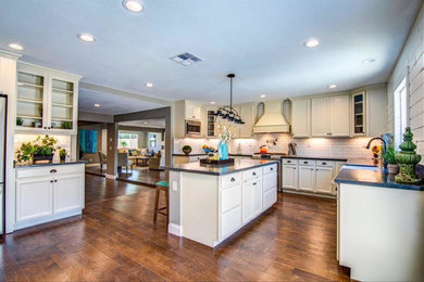 Large cottage u-shaped medium tone wood floor and brown floor open concept kitchen photo in Sacramento with a farmhouse sink, recessed-panel cabinets, white cabinets, white backsplash, subway tile backsplash, stainless steel appliances and an island