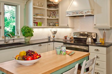Inspiration for a coastal l-shaped kitchen in Portland Maine with a submerged sink, recessed-panel cabinets, white cabinets, white splashback, metro tiled splashback, stainless steel appliances and an island.