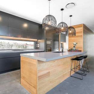 Photo of a mid-sized contemporary galley eat-in kitchen in Brisbane with a drop-in sink, flat-panel cabinets, black cabinets, mirror splashback, black appliances, concrete floors, multiple islands and grey floor.