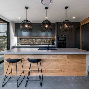Contemporary galley kitchen in Brisbane with an undermount sink, flat-panel cabinets, black cabinets, concrete benchtops, window splashback, black appliances, concrete floors, with island, grey floor and grey benchtop.