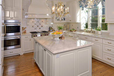 Example of a large classic u-shaped medium tone wood floor eat-in kitchen design in Houston with an undermount sink, raised-panel cabinets, white cabinets, granite countertops, white backsplash, ceramic backsplash, stainless steel appliances and an island