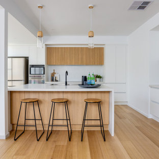 Inspiration for a large scandinavian u-shaped kitchen in Melbourne with an undermount sink, recessed-panel cabinets, white cabinets, quartz benchtops, grey splashback, porcelain splashback, stainless steel appliances, medium hardwood floors, with island and white benchtop.