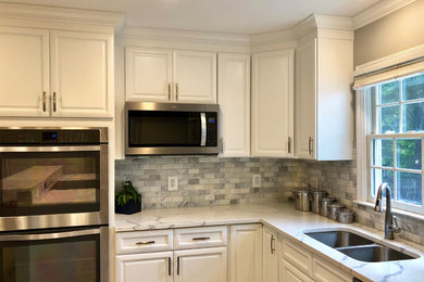 Inredning av ett klassiskt avskilt, stort vit vitt l-kök, med en dubbel diskho, skåp i shakerstil, vita skåp, bänkskiva i kvarts, vitt stänkskydd, stänkskydd i marmor, rostfria vitvaror, klinkergolv i keramik, en köksö och grått golv