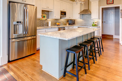 Example of a mid-sized transitional l-shaped light wood floor enclosed kitchen design in Birmingham with an undermount sink, shaker cabinets, white cabinets, granite countertops, gray backsplash, glass tile backsplash, stainless steel appliances and an island