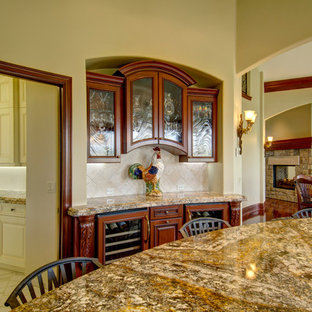 Photo of an expansive traditional u-shaped open plan kitchen in Denver with an undermount sink, louvered cabinets, medium wood cabinets, granite benchtops, white splashback, limestone splashback, stainless steel appliances, medium hardwood floors, with island and brown floor.