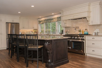 Mid-sized elegant l-shaped porcelain tile and brown floor eat-in kitchen photo in Portland Maine with a farmhouse sink, raised-panel cabinets, white cabinets, quartz countertops, beige backsplash, porcelain backsplash, stainless steel appliances and an island