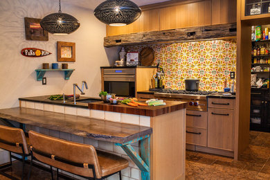 Inspiration for an eclectic galley brown floor kitchen remodel in New York with an undermount sink, flat-panel cabinets, medium tone wood cabinets, multicolored backsplash, stainless steel appliances, a peninsula and black countertops