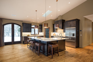 Design ideas for a large rustic l-shaped open plan kitchen in Vancouver with flat-panel cabinets, dark wood cabinets, an island, a submerged sink, granite worktops, beige splashback, stone tiled splashback, stainless steel appliances and medium hardwood flooring.
