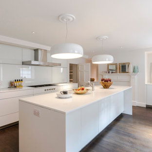 Contemporary galley kitchen in Surrey with flat-panel cabinets, white cabinets, white splashback, dark hardwood flooring, an island, brown floors and white worktops.