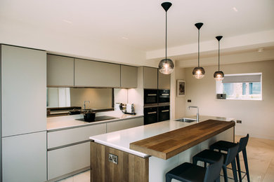 This is an example of a contemporary kitchen/diner in Cheshire with a submerged sink, quartz worktops, metallic splashback, mirror splashback, black appliances, an island and white worktops.