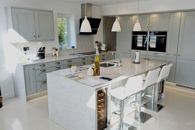 This is an example of a medium sized contemporary l-shaped kitchen/diner in West Midlands with a submerged sink, shaker cabinets, grey cabinets, quartz worktops, stone slab splashback, black appliances, porcelain flooring and an island.