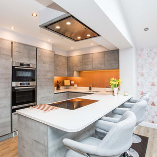 Inspiration for a contemporary u-shaped kitchen in West Midlands with a submerged sink, flat-panel cabinets, light wood cabinets, orange splashback, integrated appliances, light hardwood flooring, a breakfast bar, brown floors and white worktops.