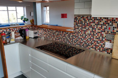 ハートフォードシャーにある広いコンテンポラリースタイルのおしゃれなキッチン (一体型シンク、フラットパネル扉のキャビネット、白いキャビネット、ステンレスカウンター) の写真