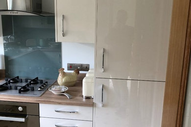Design ideas for a medium sized modern u-shaped enclosed kitchen in Kent with a single-bowl sink, flat-panel cabinets, laminate countertops, glass sheet splashback, stainless steel appliances and no island.