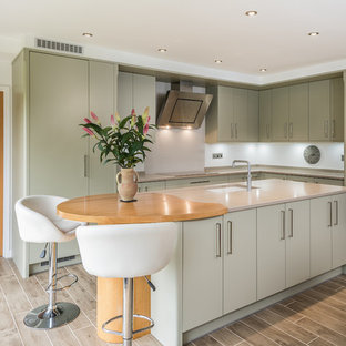 Contemporary l-shaped kitchen/diner in Other with a submerged sink, flat-panel cabinets, green cabinets, white splashback, black appliances, an island, brown floors and grey worktops.
