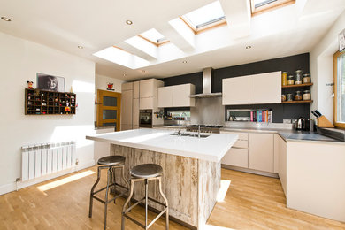Inspiration for a medium sized contemporary l-shaped kitchen in London with a double-bowl sink, flat-panel cabinets, white cabinets, stainless steel worktops, metallic splashback, light hardwood flooring, a breakfast bar and beige floors.