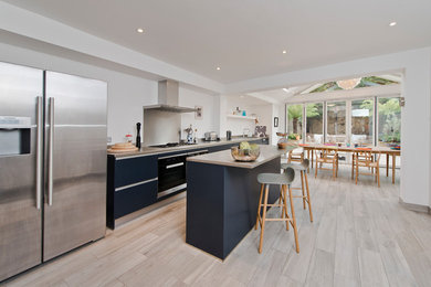 This is an example of a medium sized contemporary single-wall kitchen/diner in London with flat-panel cabinets, blue cabinets, stainless steel worktops, metallic splashback, stainless steel appliances, a breakfast bar and grey floors.