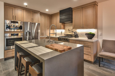 Mountain style l-shaped medium tone wood floor and gray floor kitchen photo in Salt Lake City with a farmhouse sink, shaker cabinets, medium tone wood cabinets, beige backsplash, subway tile backsplash, stainless steel appliances, an island and gray countertops