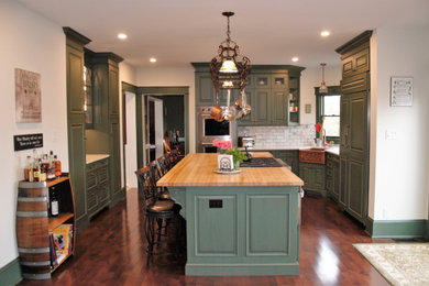 Example of a large transitional u-shaped medium tone wood floor and brown floor eat-in kitchen design in Philadelphia with a farmhouse sink, raised-panel cabinets, green cabinets, quartzite countertops, gray backsplash, marble backsplash, an island, white countertops and paneled appliances