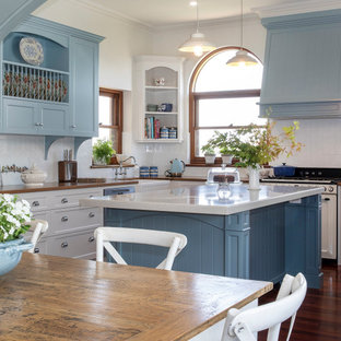Photo of a traditional u-shaped kitchen in Adelaide with a farmhouse sink, shaker cabinets, white cabinets, white splashback, coloured appliances, dark hardwood floors, with island, brown floor and white benchtop.