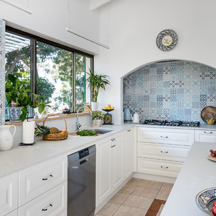 Design ideas for a mid-sized mediterranean l-shaped kitchen in Perth with an undermount sink, solid surface benchtops, blue splashback, ceramic splashback, stainless steel appliances, ceramic floors, with island, white benchtop, raised-panel cabinets, white cabinets and beige floor.