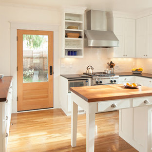 This is an example of an arts and crafts u-shaped separate kitchen in Portland with a farmhouse sink, recessed-panel cabinets, white cabinets, wood benchtops, white splashback, subway tile splashback, stainless steel appliances and medium hardwood floors.