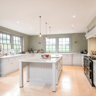 This is an example of a large country l-shaped kitchen in Hampshire with white cabinets, granite worktops, white splashback, stone slab splashback, black appliances, porcelain flooring, an island, beige floors and shaker cabinets.