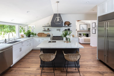 Design ideas for a large nautical l-shaped kitchen/diner in Los Angeles with a submerged sink, shaker cabinets, white cabinets, quartz worktops, white splashback, ceramic splashback, stainless steel appliances, dark hardwood flooring, an island, brown floors, grey worktops and a vaulted ceiling.