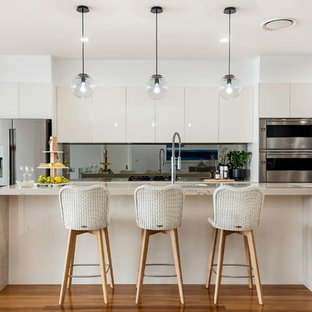 This is an example of a contemporary galley kitchen in Central Coast with beaded inset cabinets, beige cabinets, stainless steel appliances, medium hardwood floors, brown floor and beige benchtop.