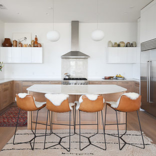 Inspiration for a scandinavian u-shaped kitchen in Portland Maine with an undermount sink, flat-panel cabinets, white cabinets, beige splashback, stone slab splashback, stainless steel appliances, light hardwood floors, with island and beige benchtop.