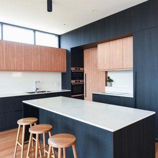 This is an example of a large contemporary l-shaped open plan kitchen in Sydney with flat-panel cabinets, black cabinets, quartz benchtops, white splashback, stone slab splashback, black appliances, medium hardwood floors, with island, brown floor, white benchtop and a double-bowl sink.