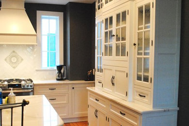 This is an example of a medium sized contemporary l-shaped open plan kitchen in DC Metro with a belfast sink, shaker cabinets, white cabinets, engineered stone countertops, white splashback, ceramic splashback, stainless steel appliances, medium hardwood flooring, an island and brown floors.