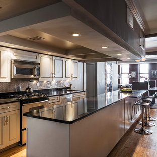 This is an example of a mid-sized industrial galley eat-in kitchen in New York with a single-bowl sink, louvered cabinets, grey cabinets, quartz benchtops, metallic splashback, ceramic splashback, stainless steel appliances, medium hardwood floors, with island and black benchtop.