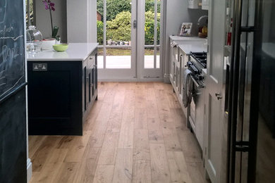 Example of a mid-sized eclectic single-wall medium tone wood floor and brown floor eat-in kitchen design in London with a farmhouse sink, shaker cabinets, gray cabinets, quartzite countertops, white backsplash, ceramic backsplash and an island