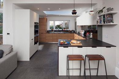 Photo of a medium sized victorian u-shaped open plan kitchen in London with a built-in sink, flat-panel cabinets, medium wood cabinets, integrated appliances, ceramic flooring, a breakfast bar, grey floors and black worktops.