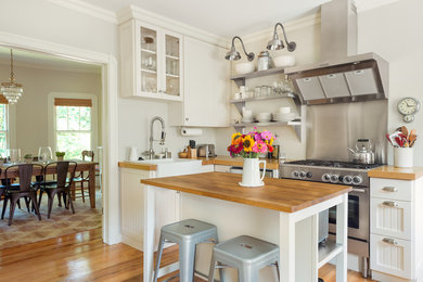 Foto på ett mellanstort lantligt l-kök, med skåp i shakerstil, vita skåp, träbänkskiva, en köksö, ljust trägolv, en rustik diskho och rostfria vitvaror