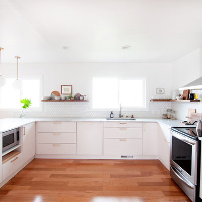 Mid-sized 1950s u-shaped medium tone wood floor kitchen photo in Denver with flat-panel cabinets, white cabinets, marble countertops, white backsplash, porcelain backsplash, stainless steel appliances, a peninsula and an undermount sink
