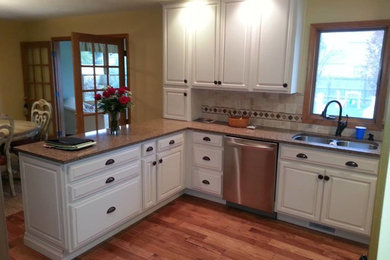 Inspiration for a mid-sized timeless u-shaped medium tone wood floor eat-in kitchen remodel in Indianapolis with a double-bowl sink, raised-panel cabinets, white cabinets, granite countertops, beige backsplash, stone tile backsplash, stainless steel appliances and a peninsula