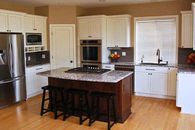 Klassisk inredning av ett mellanstort kök, med en dubbel diskho, skåp i shakerstil, vita skåp, granitbänkskiva, grått stänkskydd, stänkskydd i keramik, rostfria vitvaror, ljust trägolv och en köksö