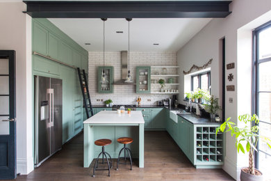 Inspiration for a large traditional u-shaped kitchen in London with a belfast sink, shaker cabinets, green cabinets, white splashback, metro tiled splashback, stainless steel appliances, medium hardwood flooring, an island, brown floors and black worktops.