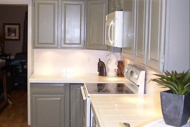Inspiration for a mid-sized timeless l-shaped medium tone wood floor enclosed kitchen remodel in Dallas with a double-bowl sink, gray cabinets, tile countertops, white backsplash, porcelain backsplash, raised-panel cabinets, white appliances and a peninsula