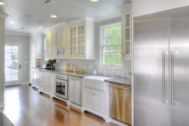 Example of a mid-sized transitional single-wall medium tone wood floor enclosed kitchen design in Los Angeles with a farmhouse sink, glass-front cabinets, white cabinets, quartzite countertops, gray backsplash, stone tile backsplash, stainless steel appliances and no island